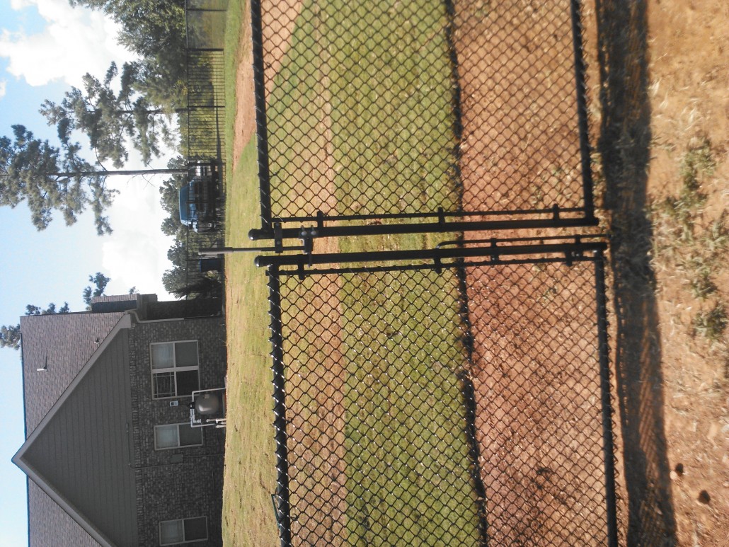 Black vinyl-coated chain link gate with metal frame providing secure entry to a fenced yard