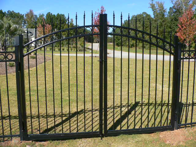 Custom ornamental iron entry gate with decorative scrollwork at a residential driveway entrance
