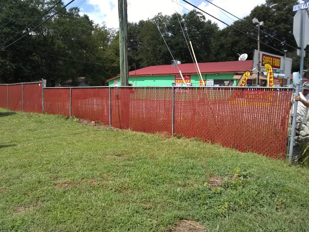 Chain link fence fitted with red privacy slats adding color and screening to a commercial property