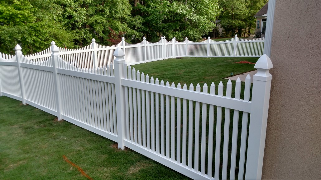 White vinyl picket fence with concave scalloped top design along a front yard walkway